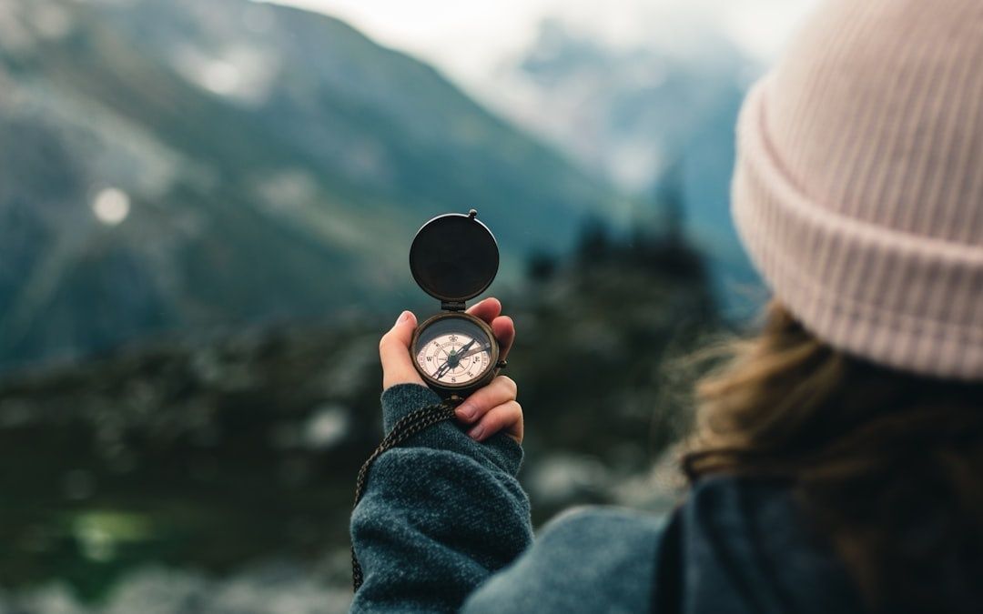 Person hält einen Kompass vor einer bergigen Landschaft in der Natur